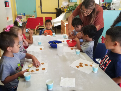 teacher at child care helping preschoolers serve snack