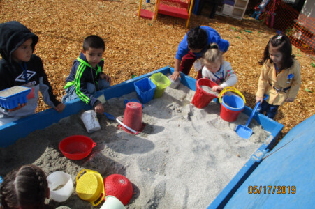 group of preschoolers playing in sandbox and childcare